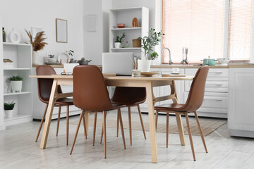 Interior of light kitchen with laptop on dining table, counters and plants