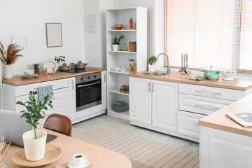Interior of light kitchen with dining table, counters and plants