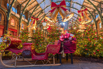Covent Garden Christmas scene features a festive sleigh, towering Christmas trees, golden bells, twinkling fairy lights, and vibrant decorations in London