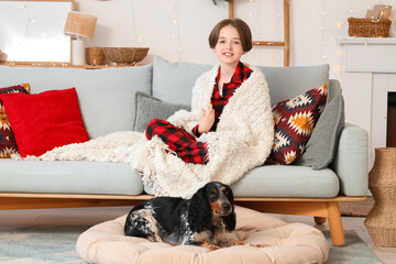 Little boy with warm blanket and cute cocker spaniel sitting on sofa at home