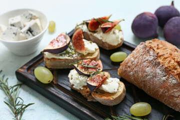Wooden board of delicious fig bruschetta with rosemary and bowl of blue cheese on light blue background, closeup