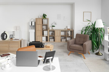 Interior of light office with workplace, armchair and shelf unit