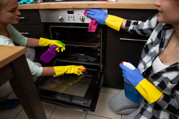 Two Women Collaboratively Cleaning an Oven Together in a Bright and Functional Kitchen Space