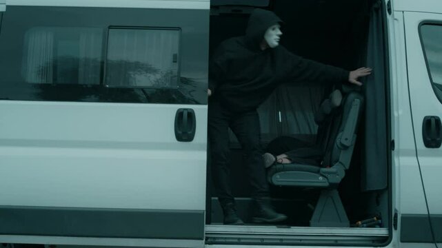 Full shot of anonymous man in mask and black clothes dragging unconscious girl into truck, looking around and shutting door, kidnapping people