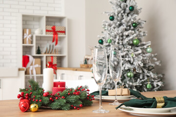 Christmas table setting with burning candles and wreath in kitchen