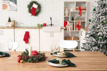 Christmas table setting with burning candles and wreath in kitchen