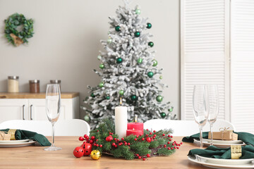 Christmas table setting with burning candles and wreath in kitchen