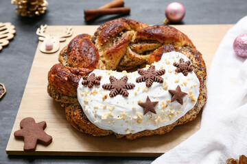 Wooden board with tasty Christmas pastry wreath on dark background, closeup