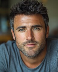 Obraz premium A man with dark hair and piercing blue eyes smiles warmly while sitting in a casual environment