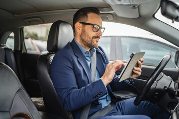 Adult businessman sit in the car and use digital tablet before go