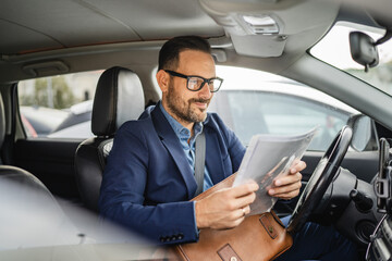 Adult businessman sit in the car and put document in his briefcase