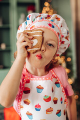 a girl child in the kitchen with a Christmas tree is preparing or cooking ginger cookies for Christmas or New year