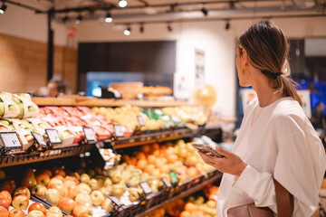 Young woman girl buyer client consumer stands in shop store supermarket choosing food buying puts in basket. Woman choose fruits.