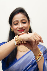 A joyful Bengali Indian woman from India, dressed in a traditional saree, is adjusting her bangles (Shaankha Pola).