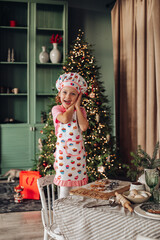 a girl child in the kitchen with a Christmas tree is preparing or cooking ginger cookies for Christmas or New year