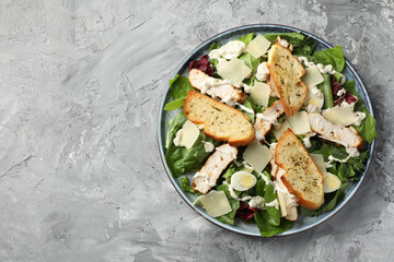 Tasty Caesar salad with chicken on gray textured table, top view. Space for text