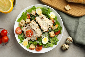 Tasty Caesar salad with chicken and tomatoes in bowl on gray textured table, flat lay