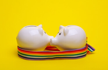Ceramic white piggy bank with rainbow tape on yellow background. LGBT. Business concept. Conceptual photo