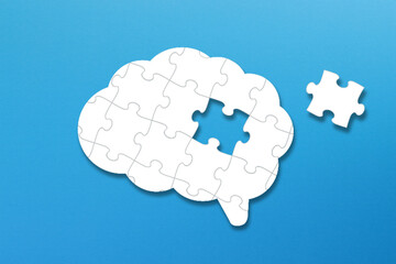 Brain shaped white jigsaw puzzle on blue background. A missing piece of the brain puzzle. Mental health and problems with memory.