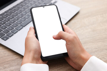 Woman unlocking smartphone with fingerprint scanner near laptop at wooden table, closeup