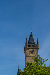 Iconic clock tower of the Old Town Hall in Prague, Czech Republic, against a clear blue sky. The tower is a historic Gothic structure with a tall, pointed roof and small golden spires at each corner.
