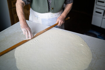 close up of grandmother rolling dough with a rolling pin. Elderly woman rolling out dough with a rolling pin
