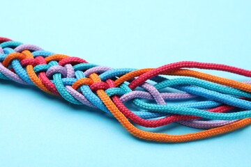 Braided colorful ropes on light blue background, closeup. Unity concept