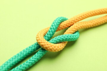 Colorful ropes tied in knot on green background, closeup. Unity concept