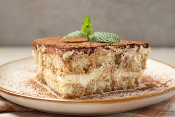 Piece of tasty tiramisu with fresh mint on beige table, closeup