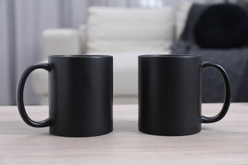 Blank black ceramic mugs on white wooden table. Mockup for design