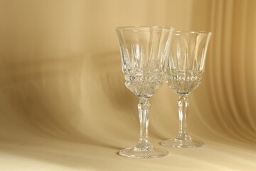 Two empty wine glasses on beige background, space for text