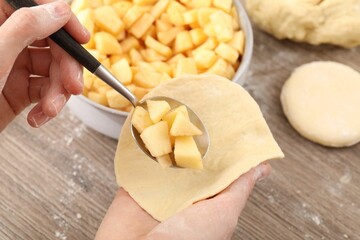 Woman making pirozhki (stuffed pastry pies) with apples at wooden table, closeup