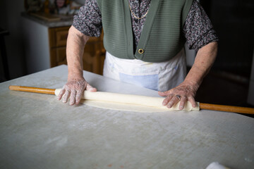 close up of grandmother rolling dough with a rolling pin. Elderly woman rolling out dough with a rolling pin