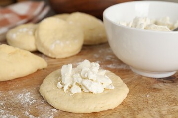 Making pirozhki (stuffed pastry pies). Pieces of dough with cottage cheese on wooden table, closeup