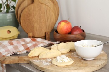 Making pirozhki (stuffed pastry pies). Pieces of dough with cottage cheese on wooden countertop, closeup