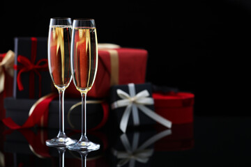 Delicious champagne in glasses and Christmas presents on black mirror surface, closeup. Space for text