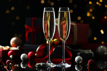 Delicious champagne in glasses and Christmas decor on black mirror surface against blurred lights, closeup