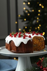 Traditional Christmas cake decorated with red currants and rosemary on table against blurred lights