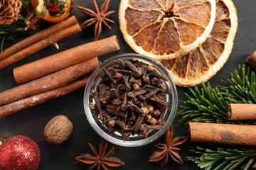 Different aromatic spices and fir tree branches on black table, flat lay. Christmas season