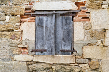 Natural stone and repaired wall with window and closed unpainted and wheathered wooden shutters or blinds in Carennac Lot Occitanie in Southern France