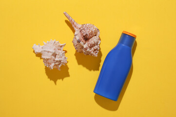 Bottle of sunscreen and shells on yellow background