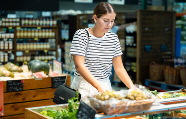 Young woman shopper choosing celery in grocery store