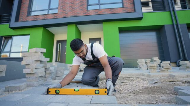 Indian construction worker uses a level tool to precisely align paving stones during installation