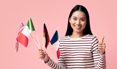 Happy Asian Female Sitting With International Flags And Laptop And Showing Thumb Up, Positive...
