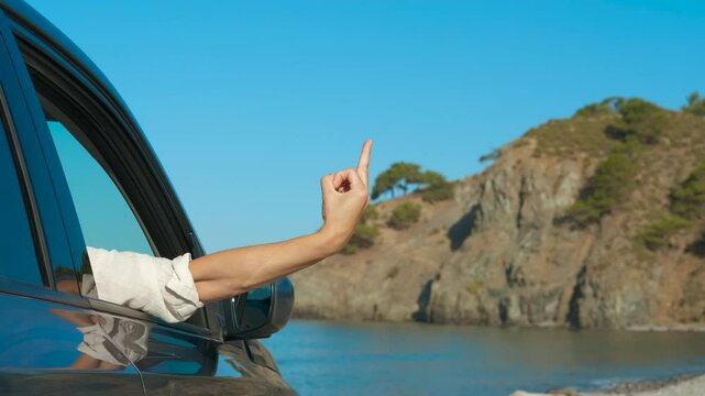 Woman in car showing middle finger gesture. Woman sticking her arm out of a car window makes an obscene gesture. The scene captures a moment of frustration during a summer road trip