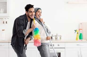 Beautiful joyful muslim young couple cleaning floor and having fun in kitchen together, full length...