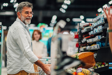 Senior man buying groceries at checkout counter in supermarket