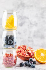 Antioxidant and anti-inflammatory fruit, pomegranate, orange and blueberries in glass jars forming a tower.