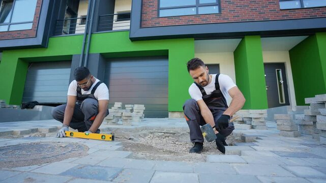 Two diverse construction workers fixing the pavestone on patio