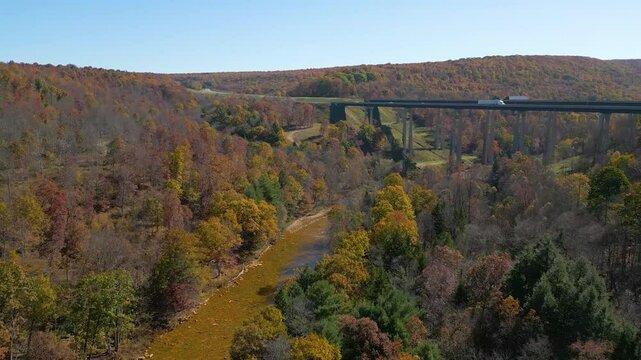 Aerial view of a highway bridge spanning across a river valley with beautiful Fall foliage, drone 4K